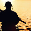 Silhouette of special forces with rifle in action during river raid in the jungle waist deep in the water. Front view, half length